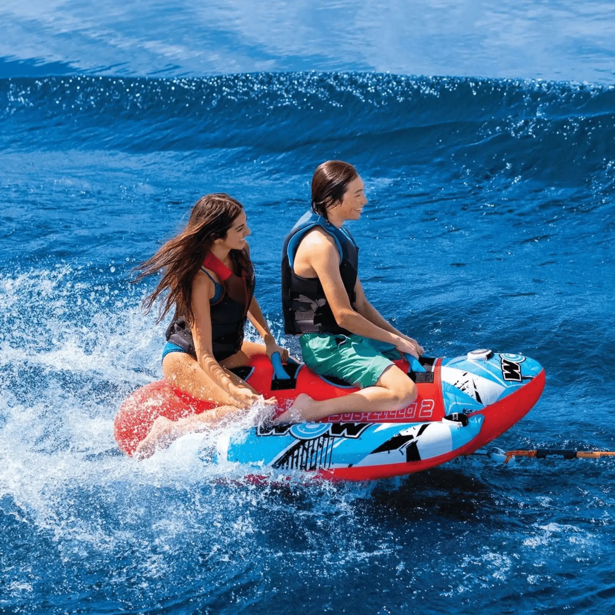 WOW Watersports Sub-Zilla 2-person towable being ridden by two riders on blue ocean waves