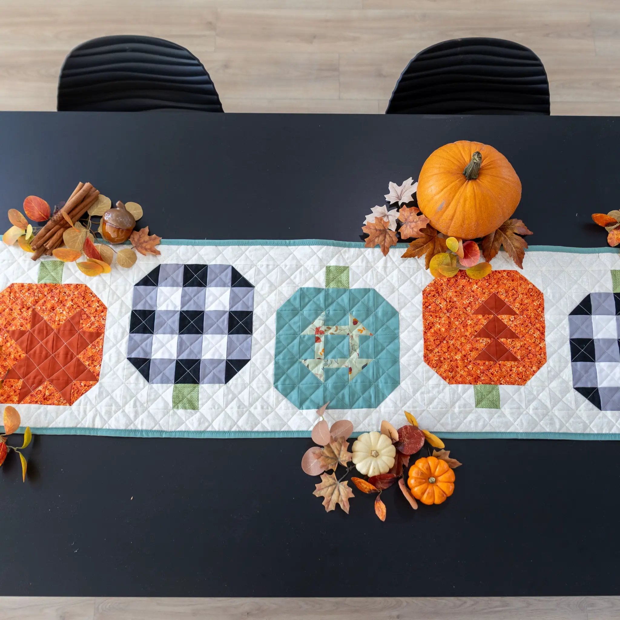 Pumpkin Patchwork Quilted Table Runner Quilt Kit on dark table with pumpkins and autumn leaves