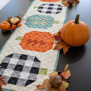 Quilt Kit: Pumpkin Patchwork Quilted Table Runner in fall colors with teal border, surrounded by pumpkins.