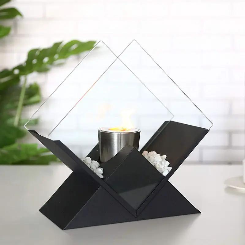 Tabletop fireplace with black geometric base, clear diamond glass panels, stainless burner, white pebble accents, flame.