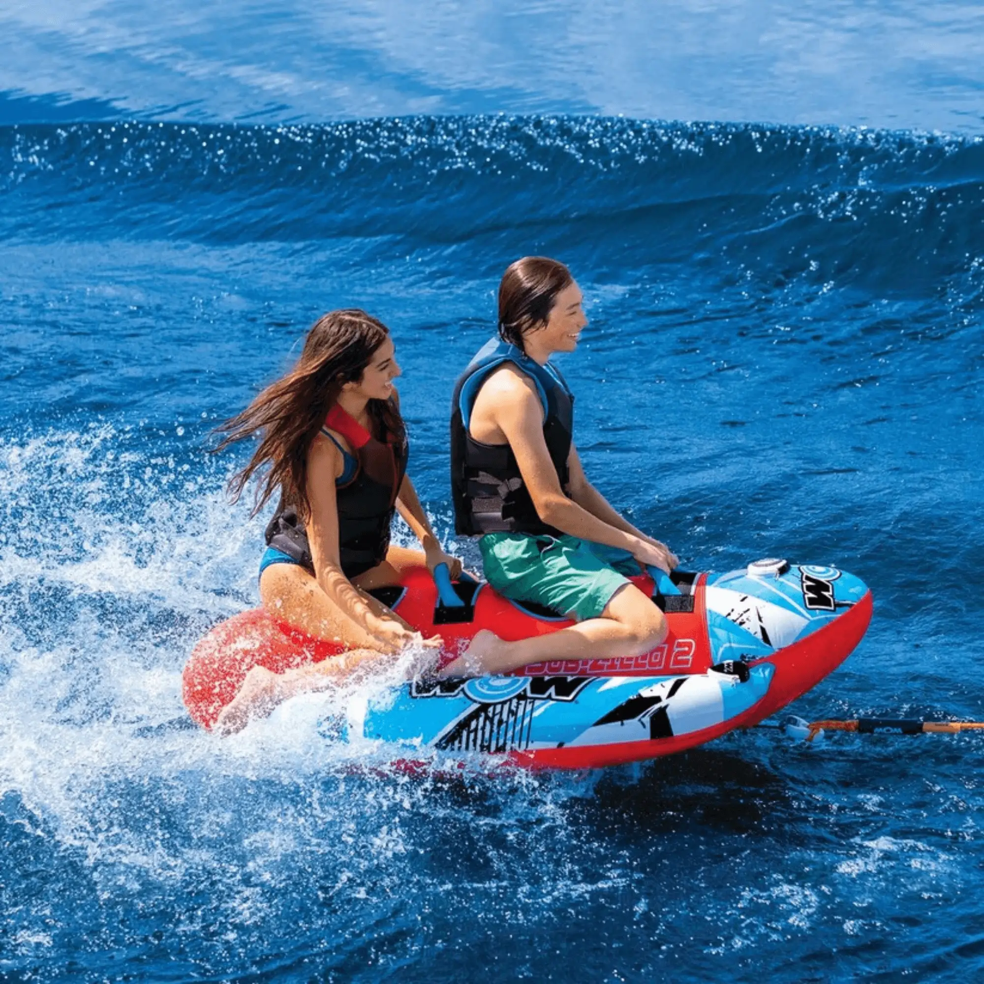 WOW Watersports Sub-Zilla 2-Person Towable; red and blue inflatable with two riders on the water