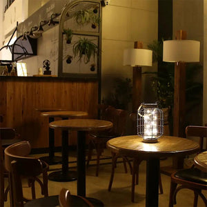 9.4-in tall battery-powered table lamp by JHY DESIGN with a metal cage on a wooden cafe table