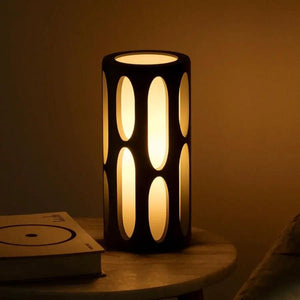 Amoeba Table Lamp, black metal cylinder with oval cutouts casting warm amber glow.
