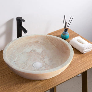 Beige travertine above-counter bathroom vessel sink on wooden vanity with a black matte faucet.
