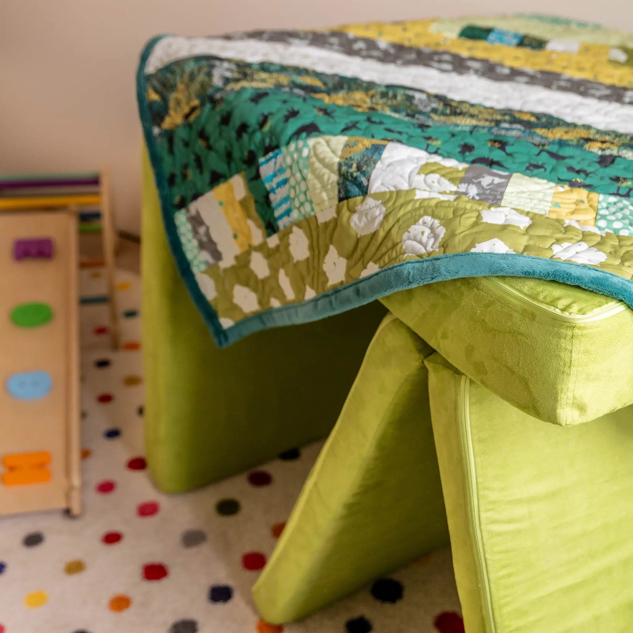 Bricks and Beams Quilt Kit on a green sofa, displaying teal, lime, and yellow patchwork fabrics.