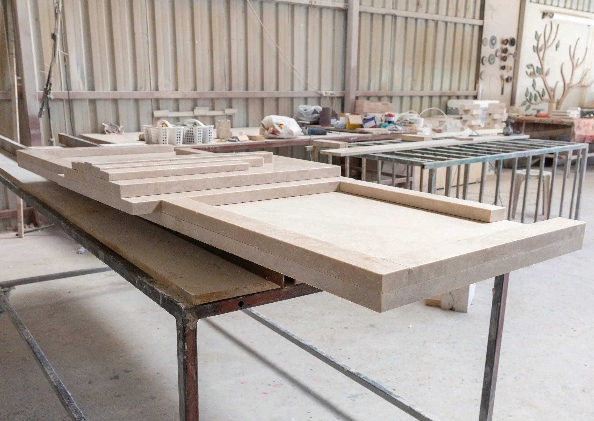 Cappuccino beige marble fireplace mantel, hand-carved Art Deco, polished; several slabs stacked on workshop table.