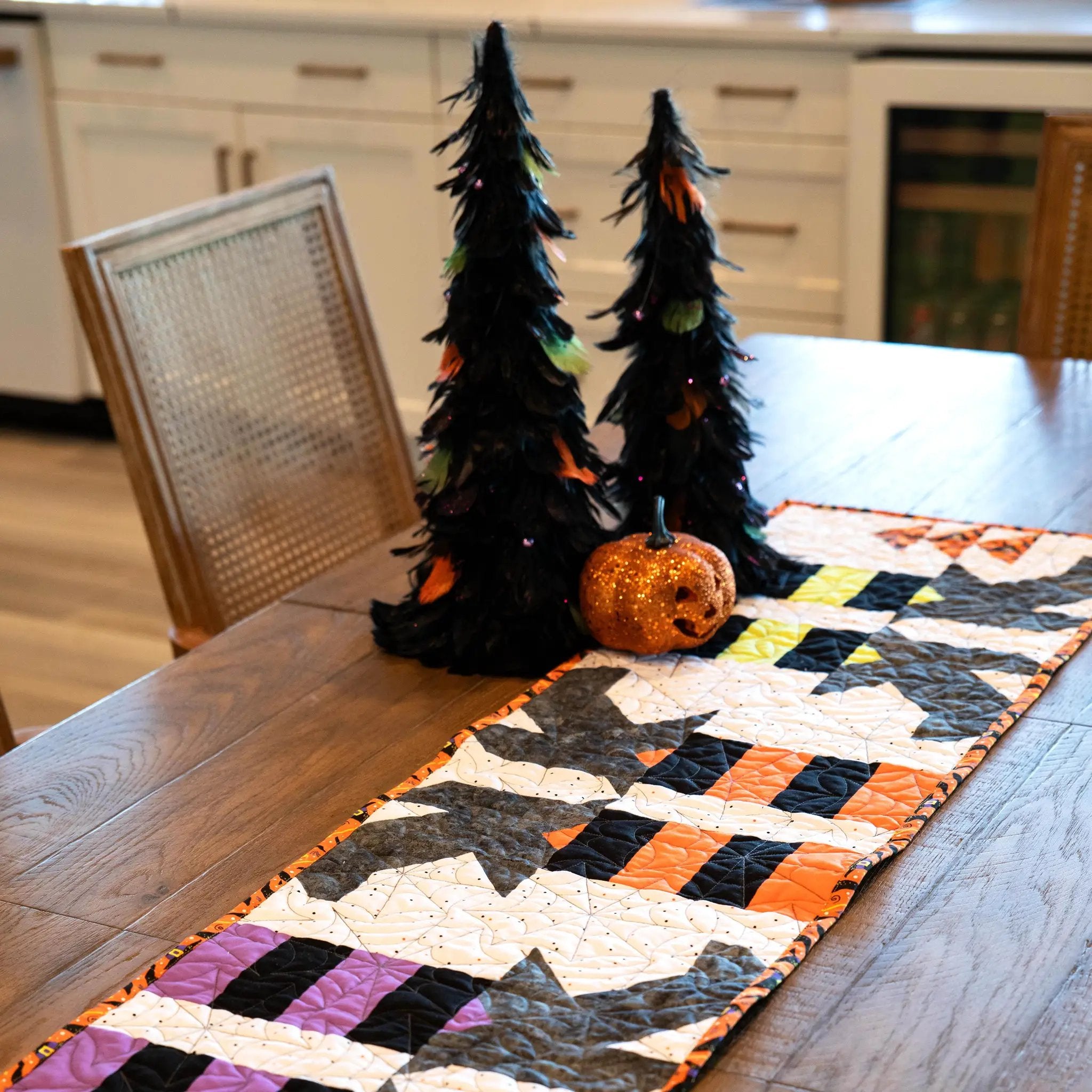 Witches Feet Table Runner Quilt Kit by Block Party Quilt Co; Halloween patchwork on a wooden table with two pumpkins.