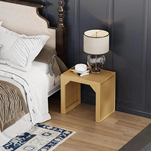 Natural wood slatted bedside table with glass lamp and books in a modern bedroom.