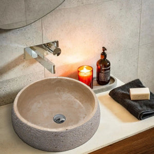 Travertine vessel sink in light beige on vanity with chrome faucet.
