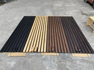 Solid wood acoustic slat wall panels broad-strip in black, natural and brown finishes laid out on a workshop floor.