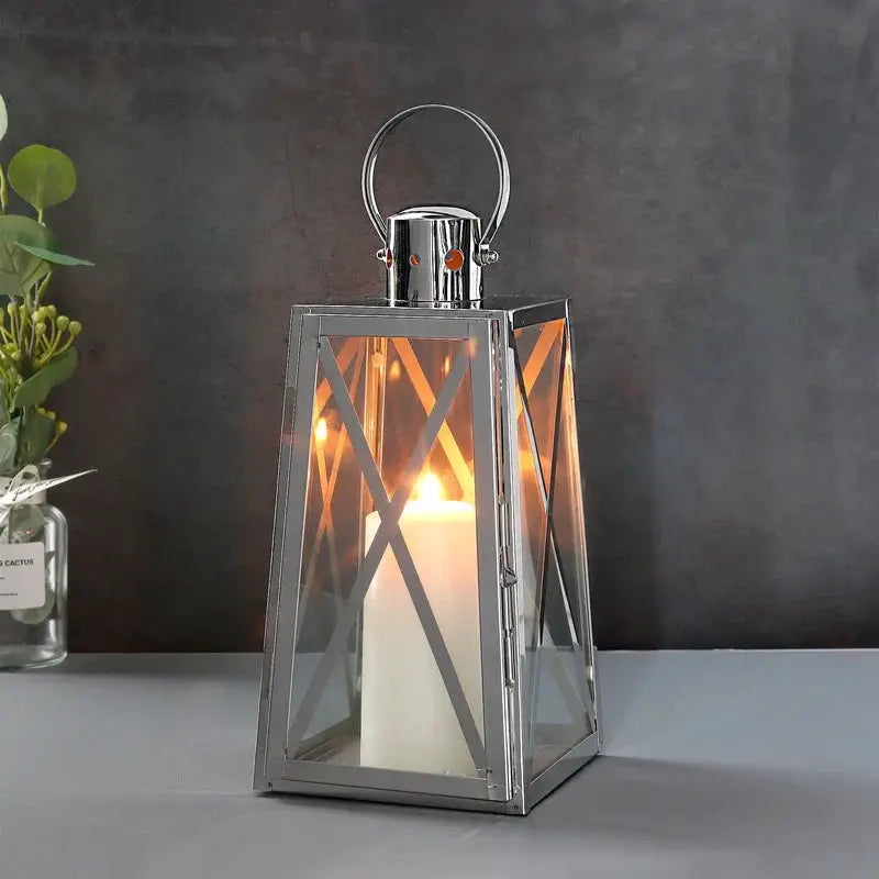 12''H Stainless Steel Decorative Lantern by JHY DESIGN with glass panels, trapezoid frame, lit candle inside