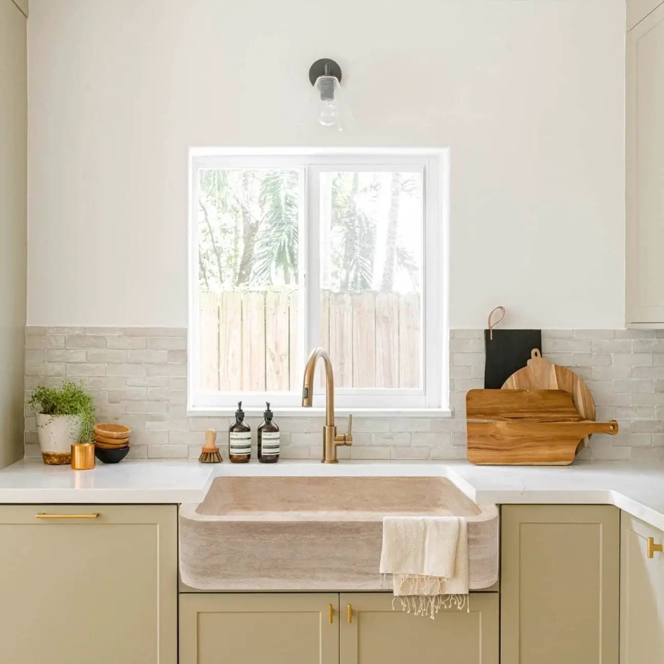 Troia Light Travertine rectangular farmhouse kitchen sink with brass faucet.