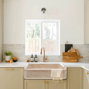 Troia Light Travertine rectangular farmhouse kitchen sink with brass faucet.