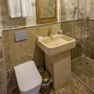 Troia Light travertine pedestal sink, beige stone, honed and filled, standalone bathroom unit beside glass shower