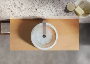 Troia Light travertine above-vanity sink; round light stone basin with chrome faucet on wood vanity.
