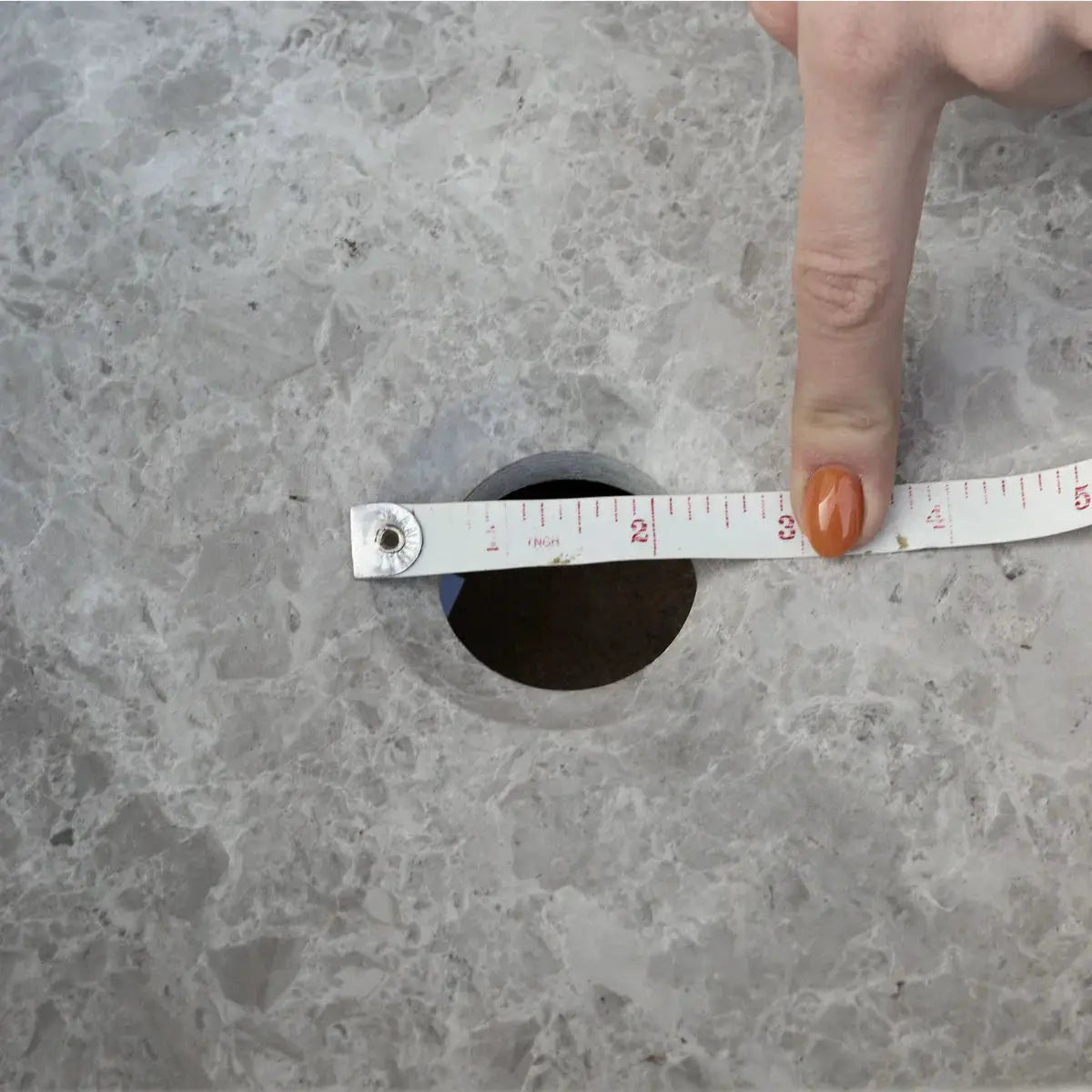 Tundra Gray Marble bathroom sink by Villohome with measuring tape across a round drain hole