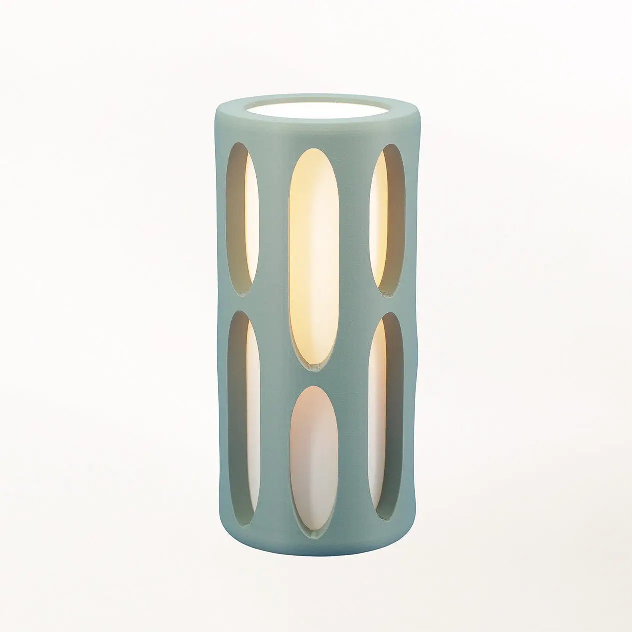 Amoeba Table Lamp, teal sculptural cylinder with vertical oval cutouts and warm interior glow by Terra Labs