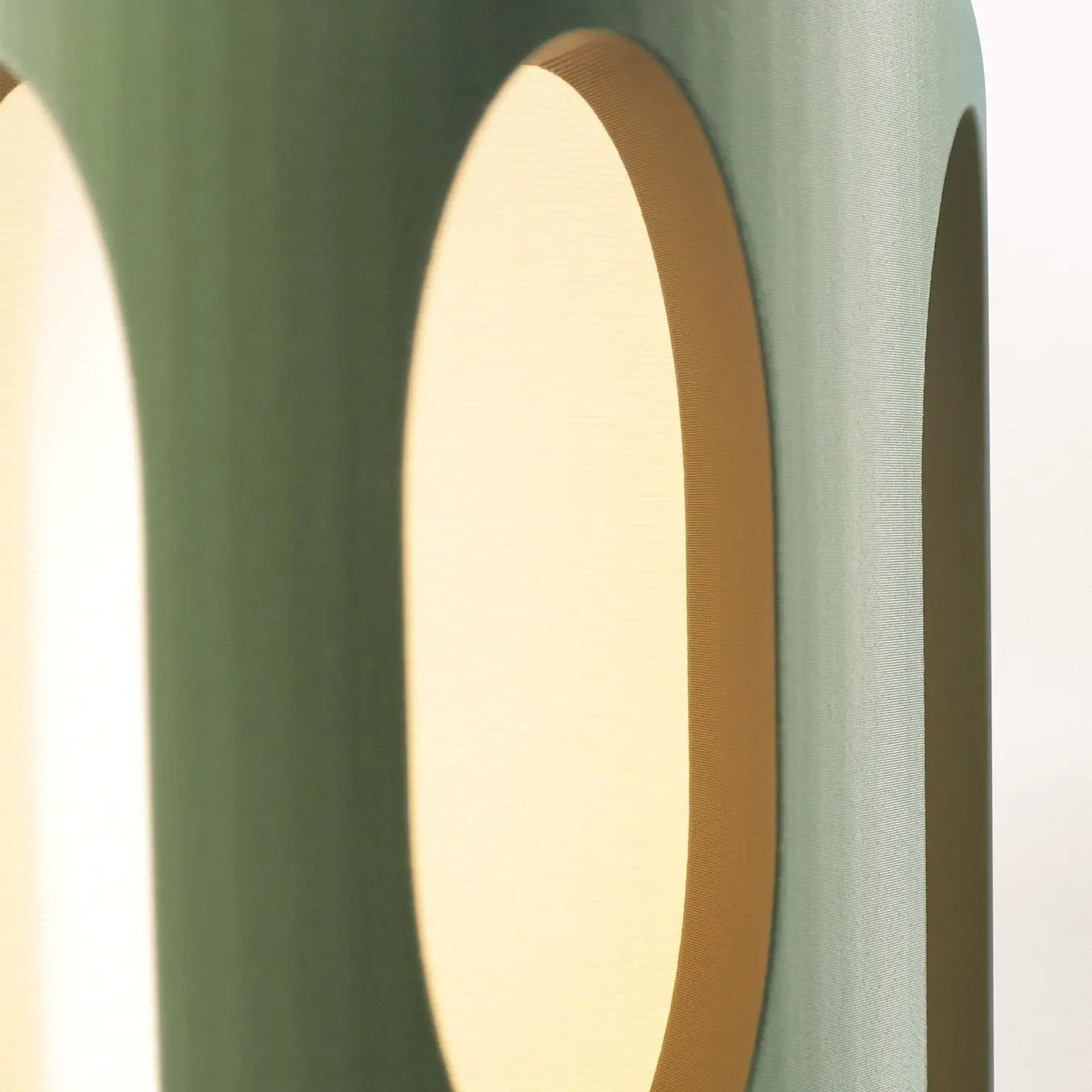 Amoeba Table Lamp by Terra Labs, teal green curved shell with warm light visible through circular openings.