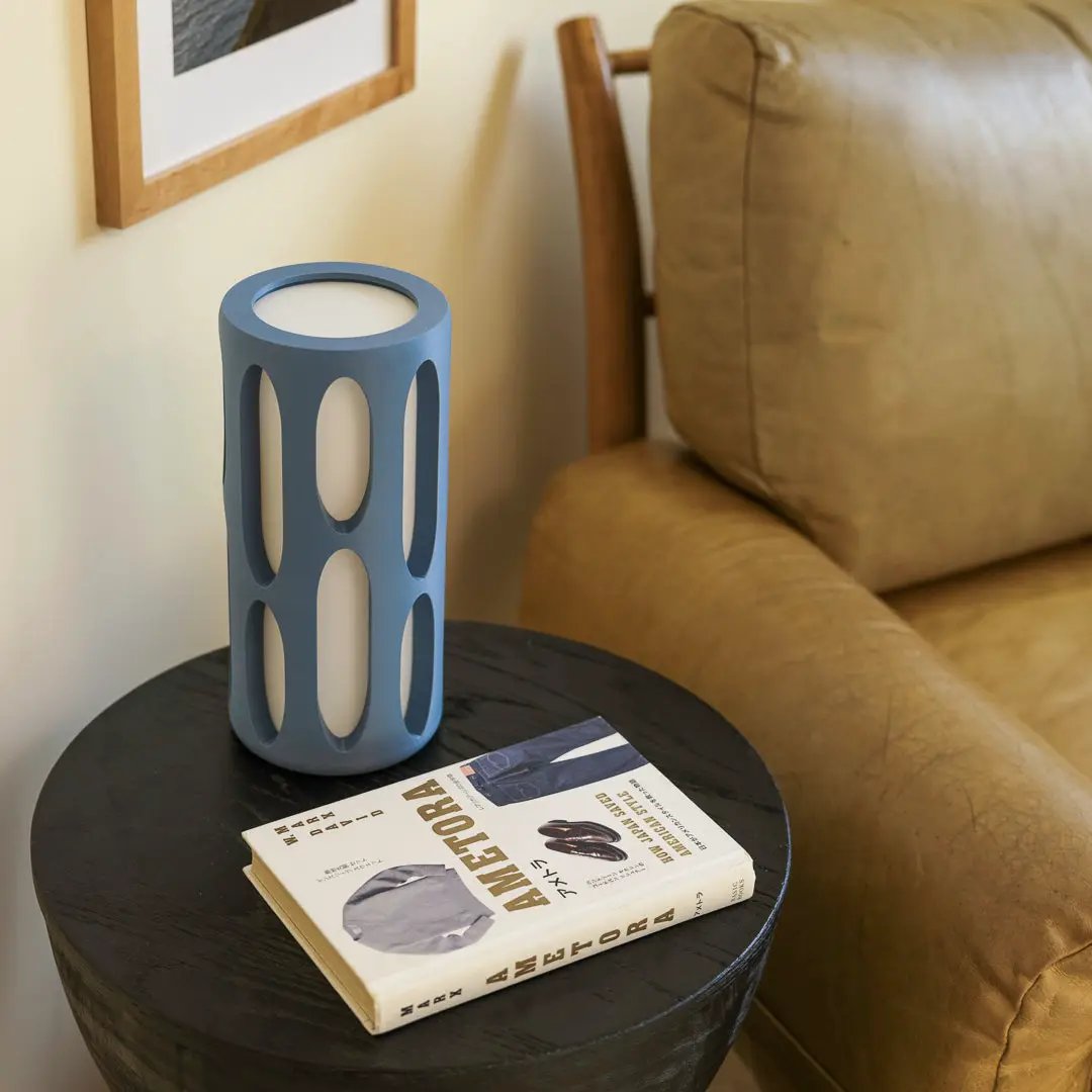 Amoeba table lamp by Terra Labs; blue cylindrical lamp with oval cutouts on a round black table.