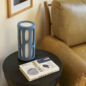 Amoeba table lamp by Terra Labs; blue cylindrical lamp with oval cutouts on a round black table.
