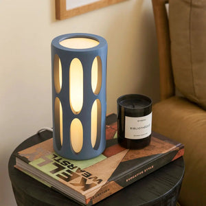 Amoeba Table Lamp by Terra Labs; blue lamp with elongated oval cutouts, warm glow on a round table beside a candle.