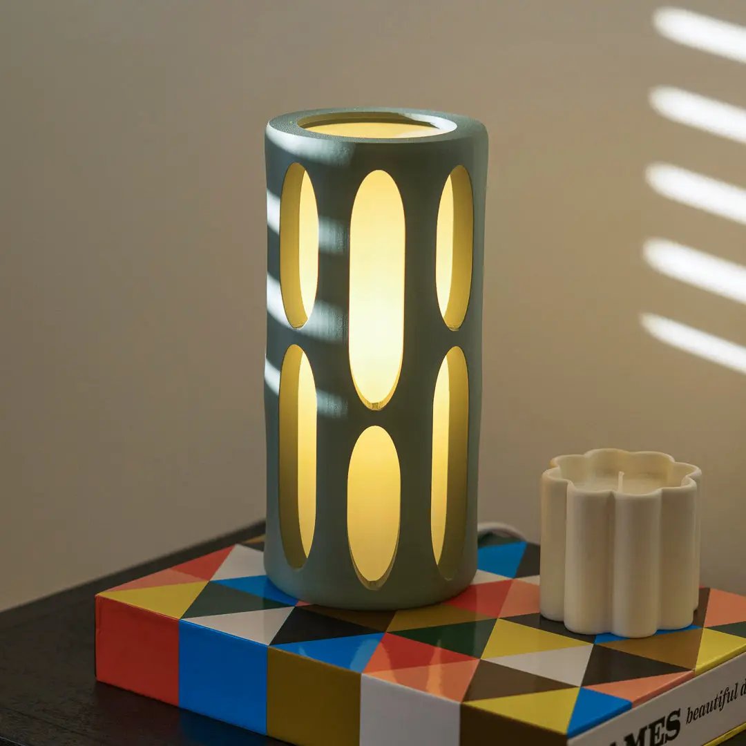 Amoeba table lamp, teal cylindrical body with oval cutouts and warm yellow glow