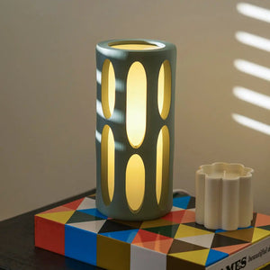 Amoeba table lamp, teal cylindrical body with oval cutouts and warm yellow glow
