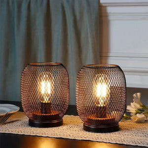 Set of 2 tall battery-powered outdoor table lamps with copper-tone metal mesh cages and warm glow bulbs.