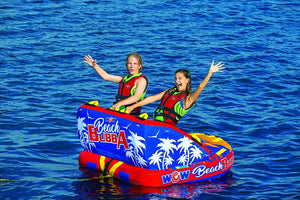 WOW Beach Bubba 2-person towable raft; blue with palm tree graphics, red trim, two riders in life jackets on blue water.