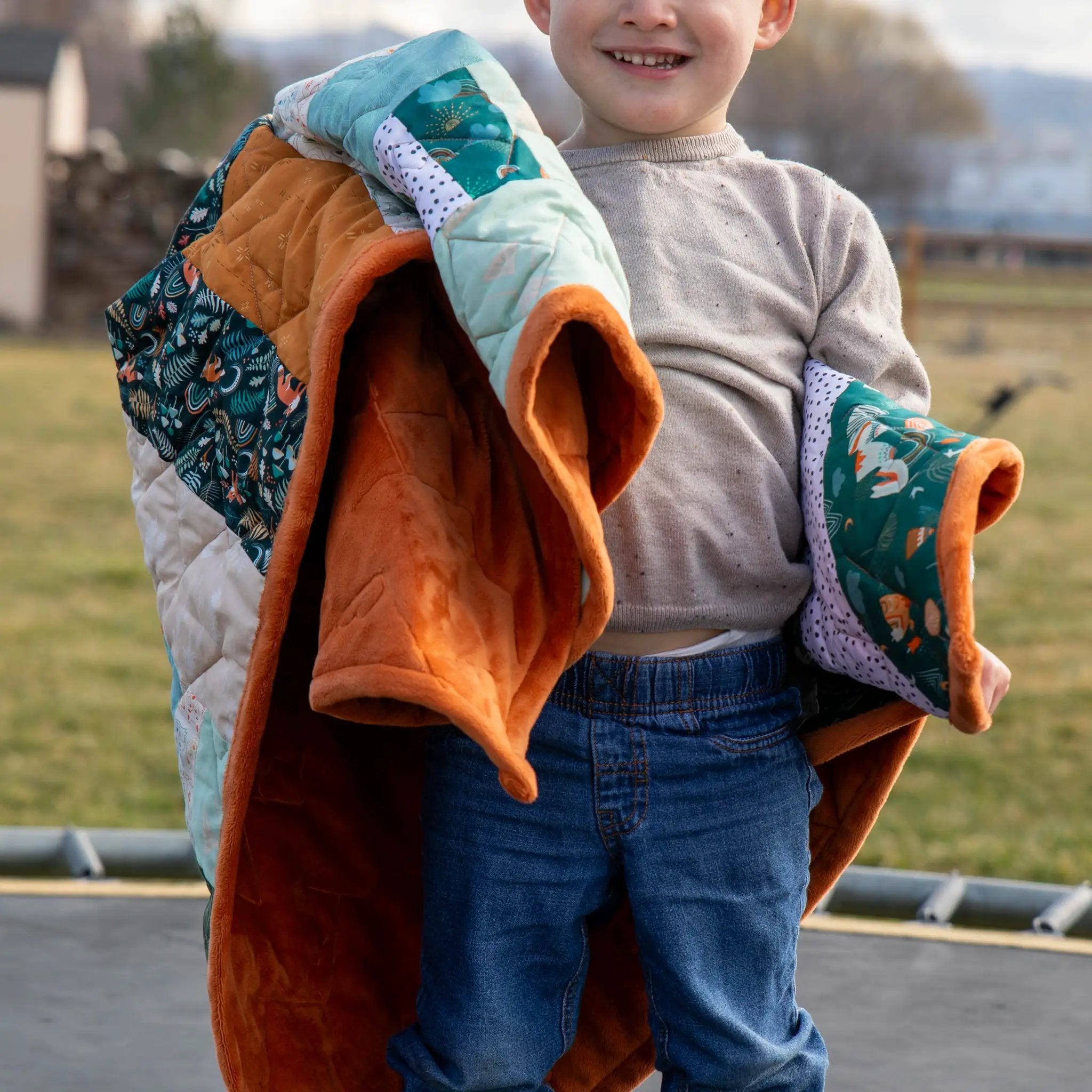 Bricks and Beams Quilt Kit Timberline by Block Party Quilt Co; teal and orange patchwork quilt carried by a child outdoors