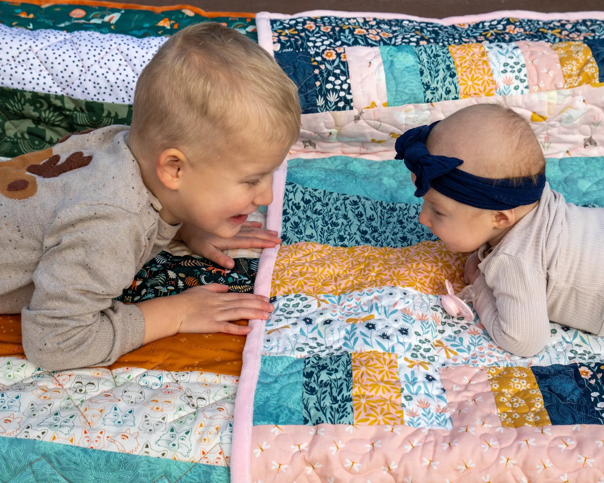 Bricks and Beams Quilt Kit Timberline by Block Party Quilt Co; colorful patchwork quilt with two babies on it