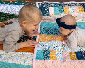 Bricks and Beams Quilt Kit Timberline by Block Party Quilt Co; colorful patchwork quilt with two babies on it