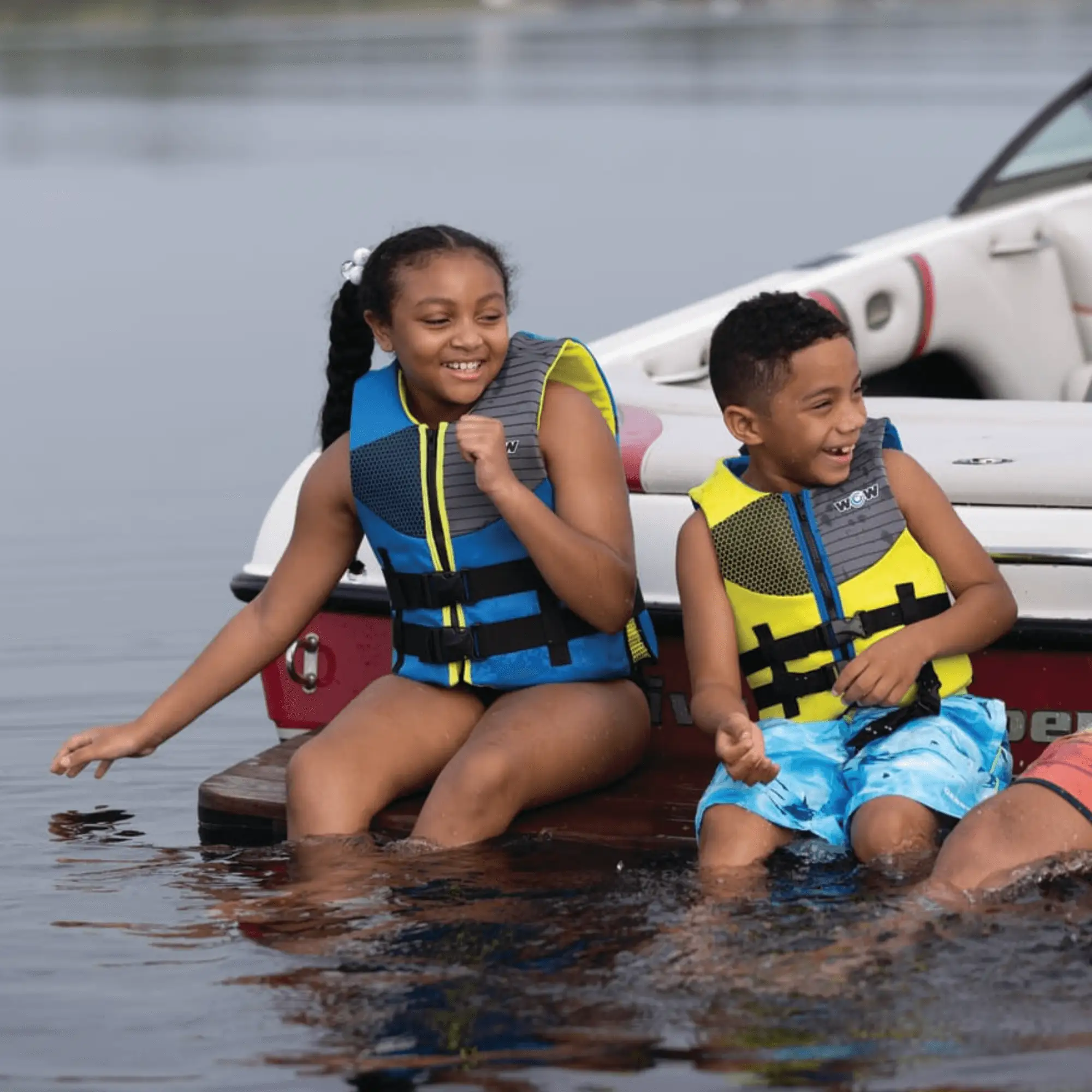 WOW Watersports PFD life jackets for children worn by two kids on a boat; blue and neon yellow vests with black straps
