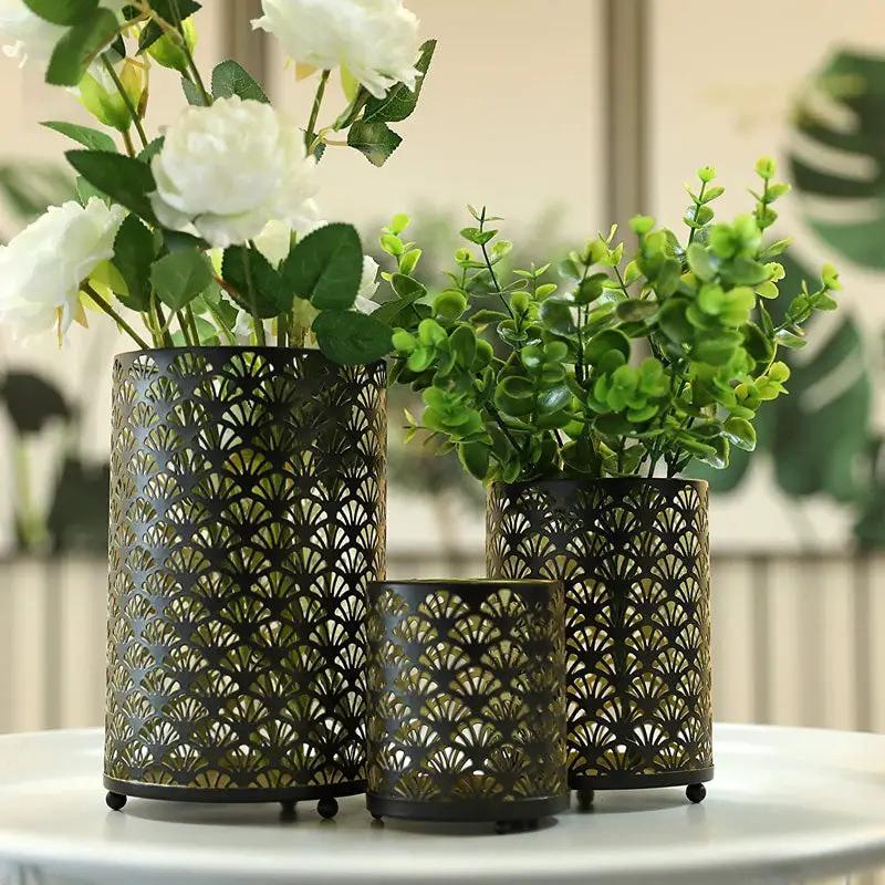 Set of 3 metal hurricane lanterns with black perforated pattern and gold interior, with faux flowers and greenery.