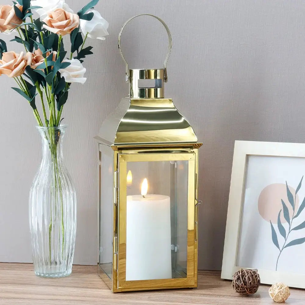 12.5-inch high decorative lantern, gold metal with glass panels and a lit white pillar candle inside
