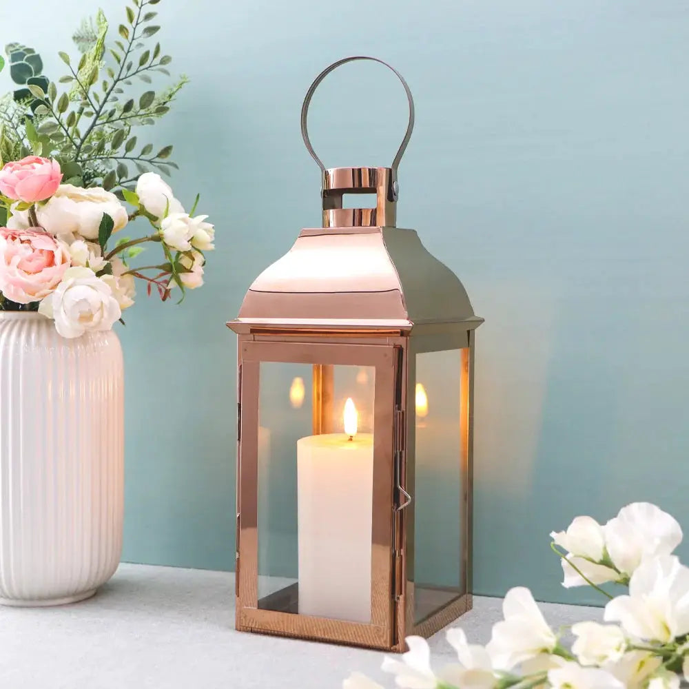 12.5-inch high decorative lantern with copper finish, glass panels, and a lit candle inside