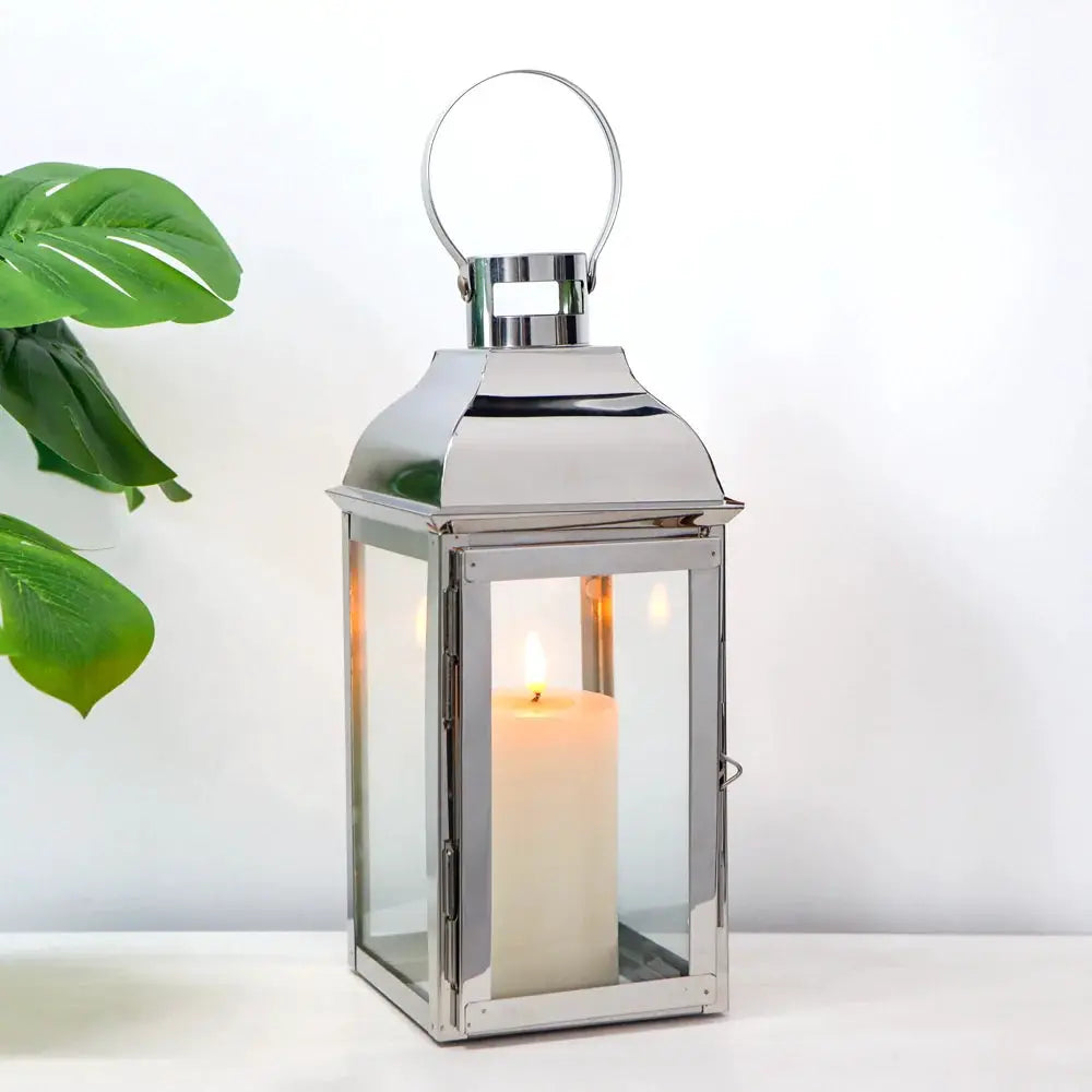 12.5-inch high decorative lantern by JHY DESIGN with a silver metal frame, glass panels, and a lit candle inside.