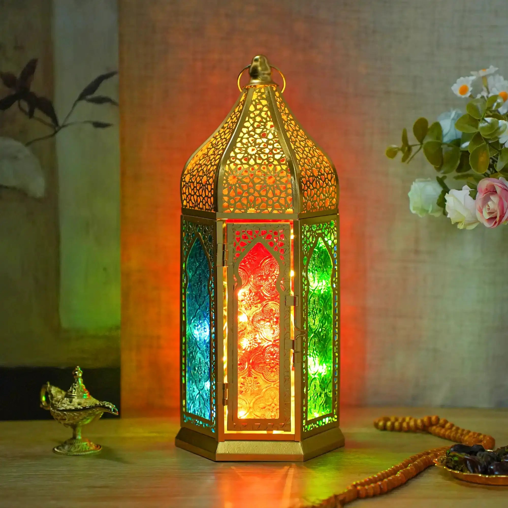 12-inch gold hexagonal Moroccan candle lantern with intricate lattice panels and multicolored glass, lit from inside.