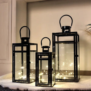 Set of 3 black stainless steel candle lanterns with glass panels and warm string lights