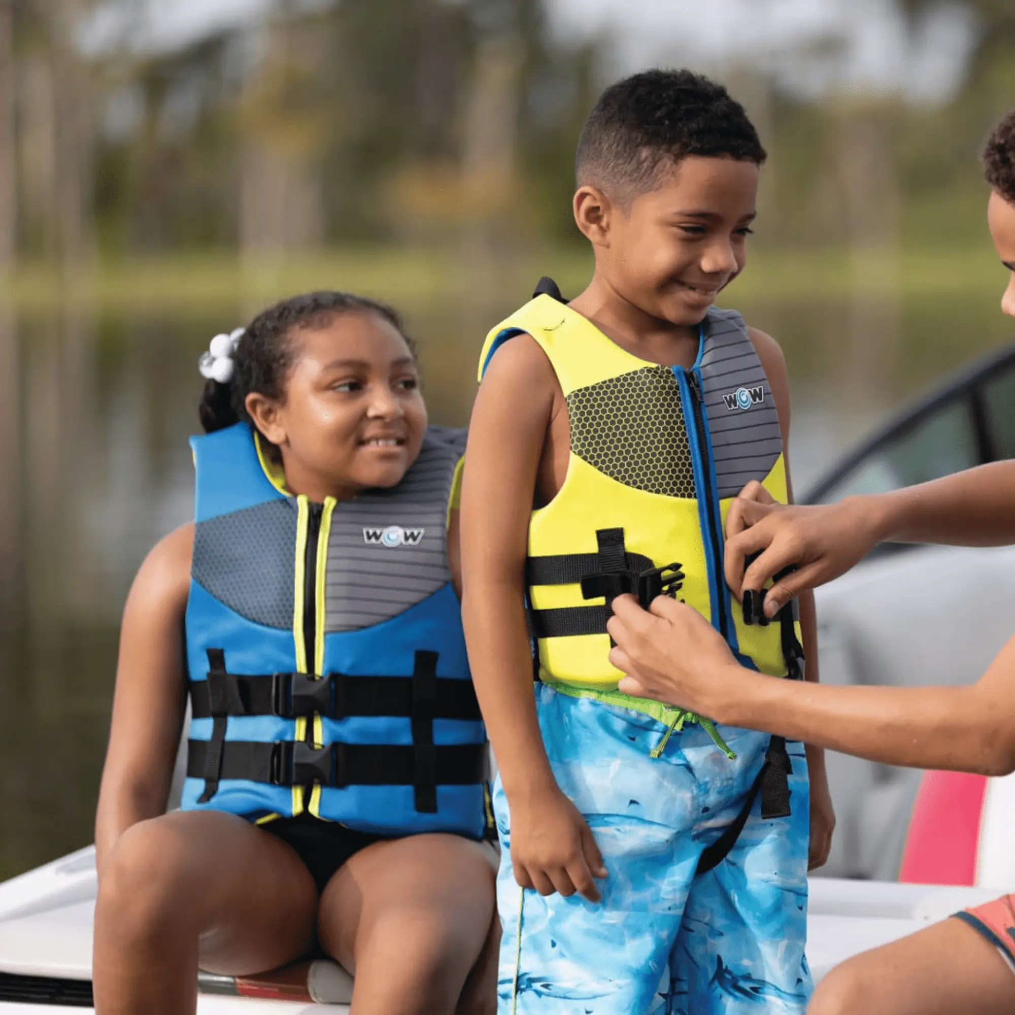 Life jackets: three kids wearing WOW brand PFDs in yellow, gray, and blue on a boat.