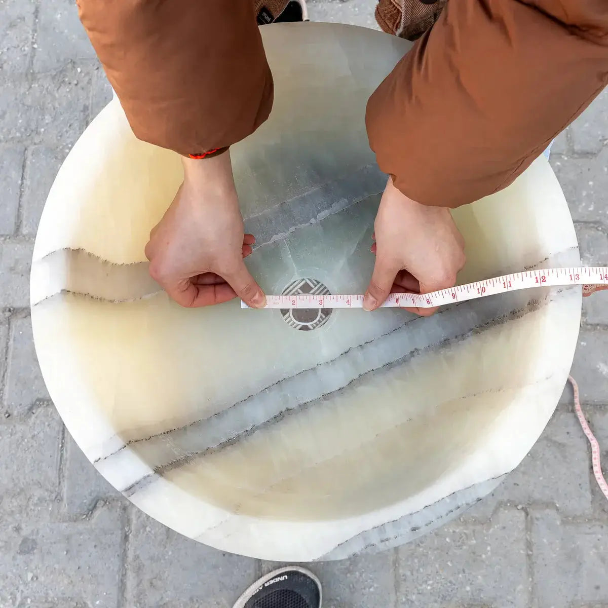 Green translucent onyx bathroom vessel sink on a round vanity top, being measured with a tape across its diameter.