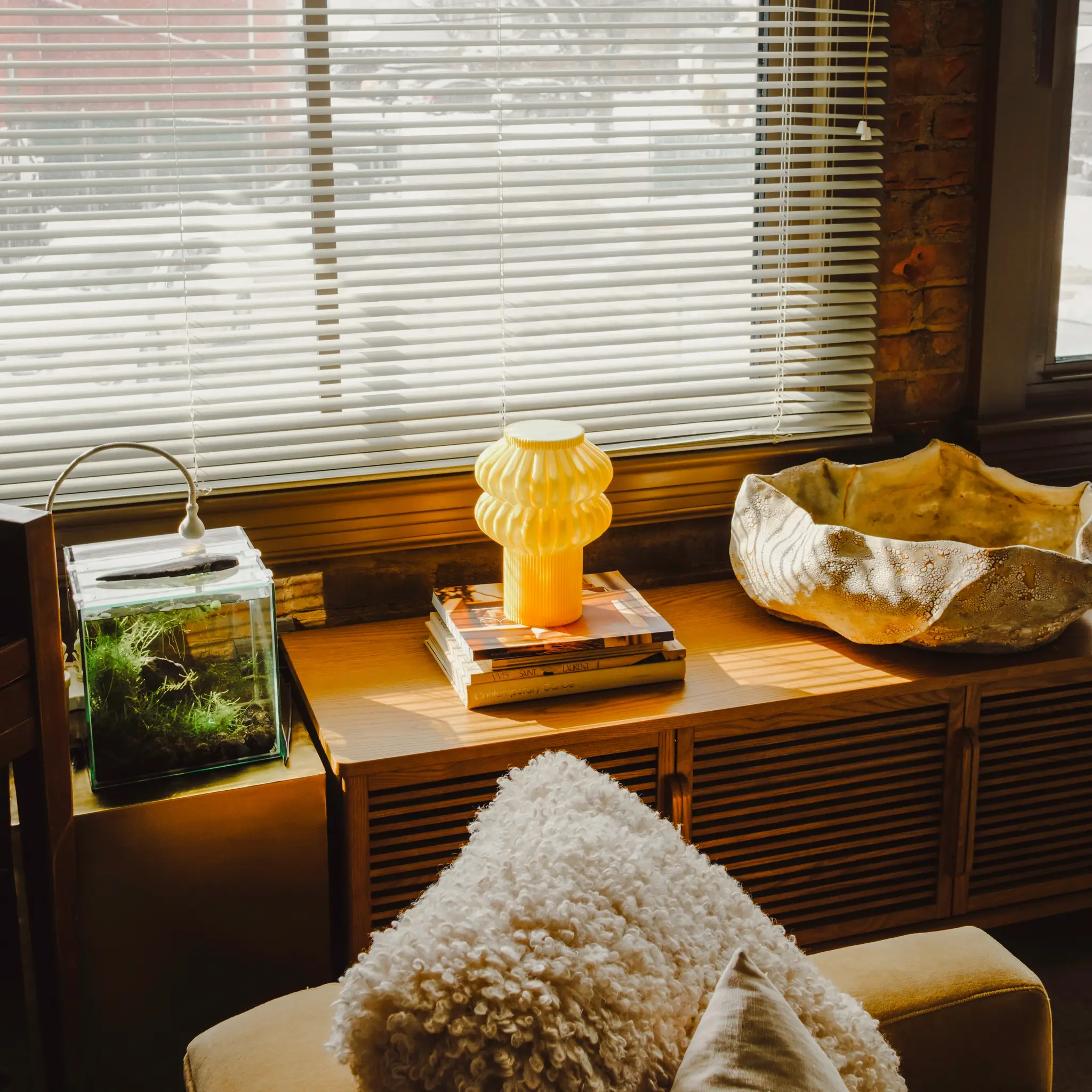Oppi Table Lamp by Terra Labs; yellow ribbed glass table lamp on a wooden console by a window.