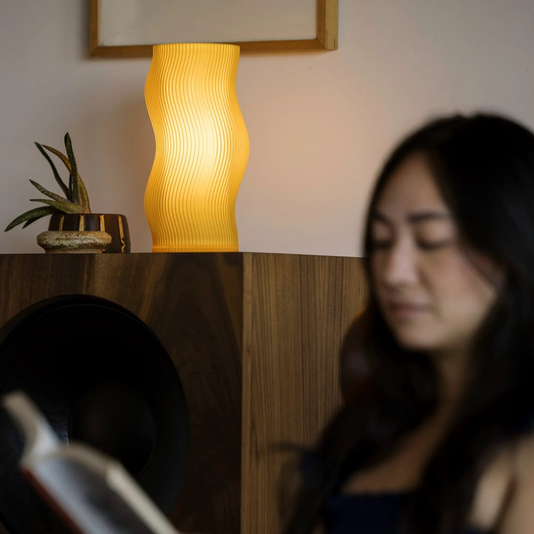 Woogie table lamp by Terra Labs, yellow ribbed curved shade on a wooden shelf.