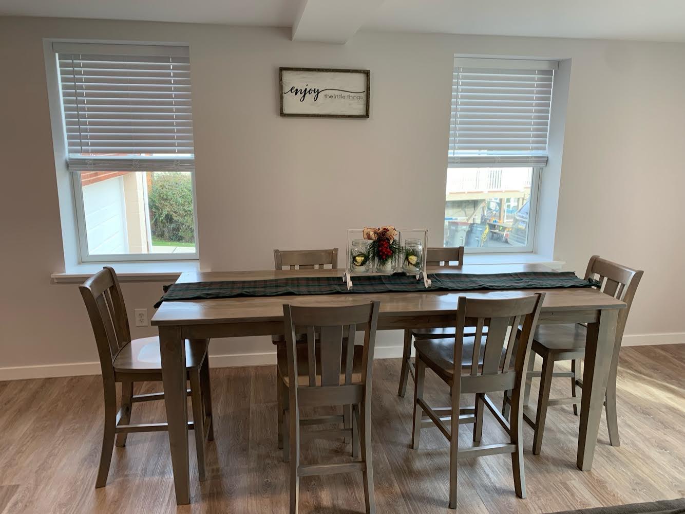 San Remo style stools around a long light gray wooden dining table in a bright dining room.