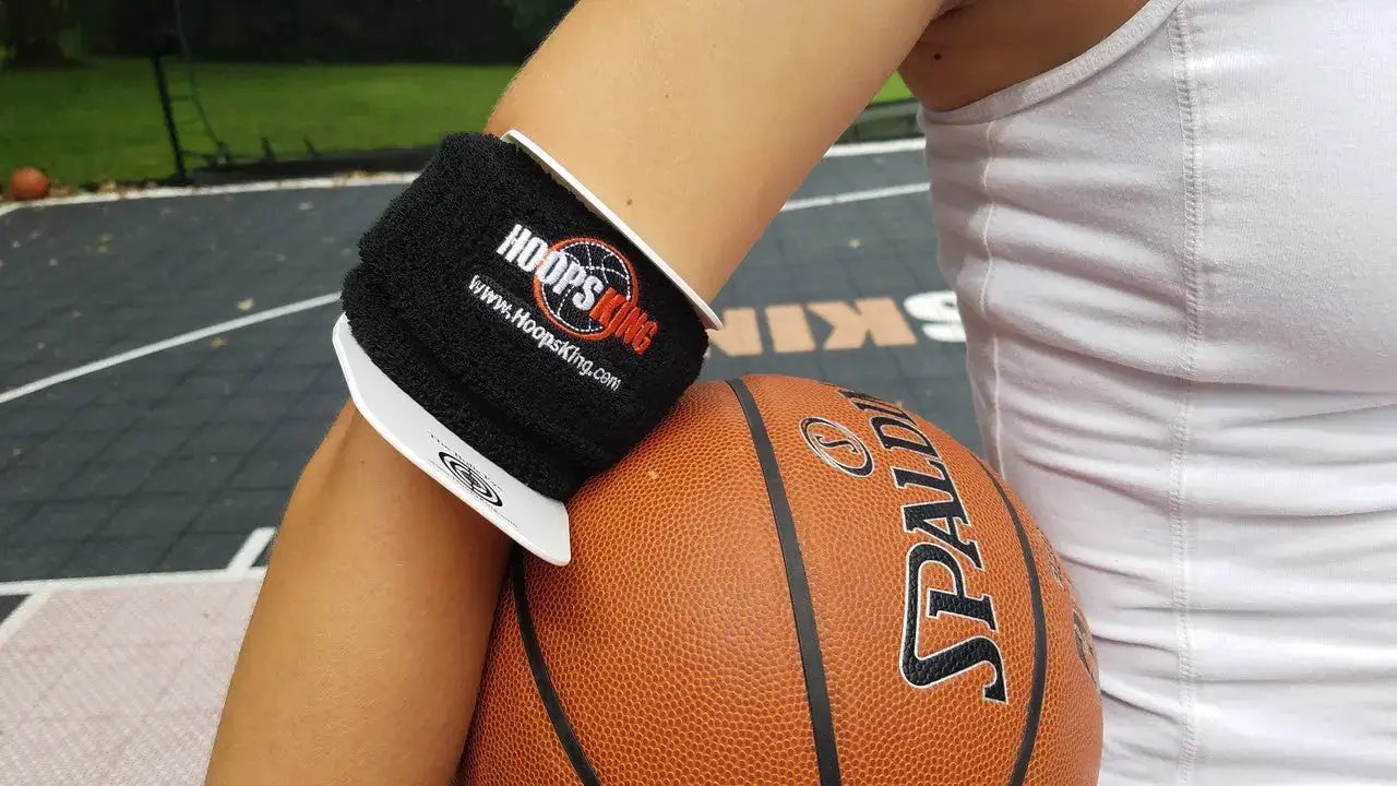 Bulls Eye Basketball Shooting Aid by HoopsKing on a black wrist strap with white trim beside an orange basketball.