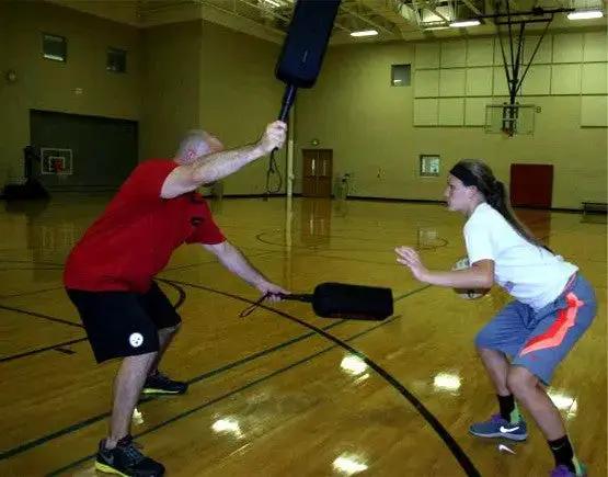 Defender Extender Basketball Training Pads in use during a gym drill by two players; black pad held between them.
