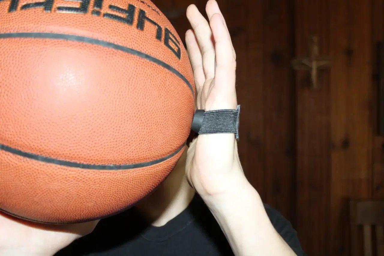 HoopsKing No Palm Dribbling & Shooting Palm Aid (Pair) on a hand with a black strap gripping an orange basketball.