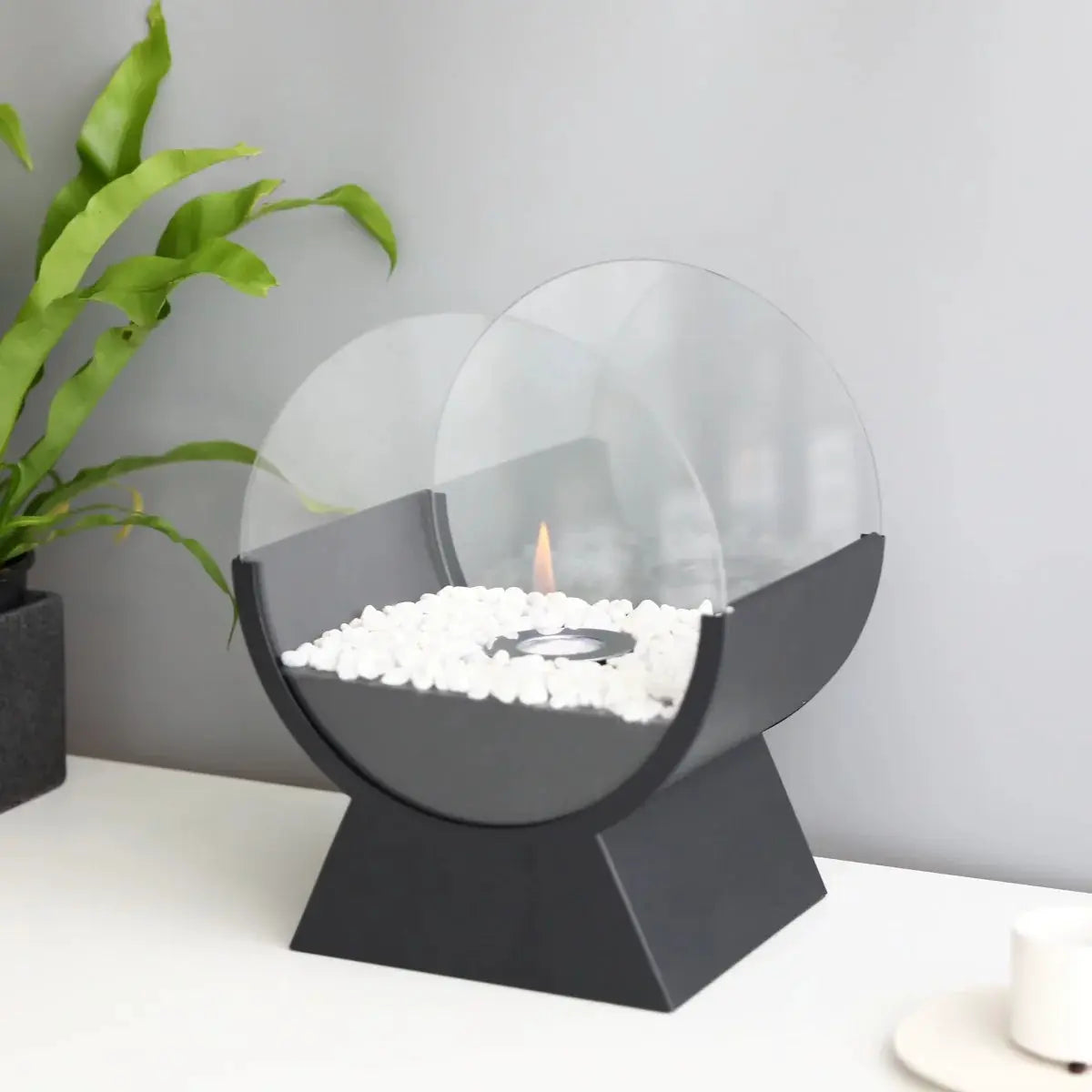 13.5-inch tall portable tabletop fireplace by JHY DESIGN with round glass guard, black base, and white stones
