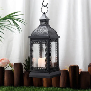 Rustic black metal candle lantern with glass panels and intricate scrollwork, hanging from a hook.
