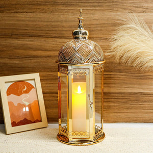 Moroccan candle lantern, gold, 15-inch hexagonal metal frame with glass panels and a lit candle inside.